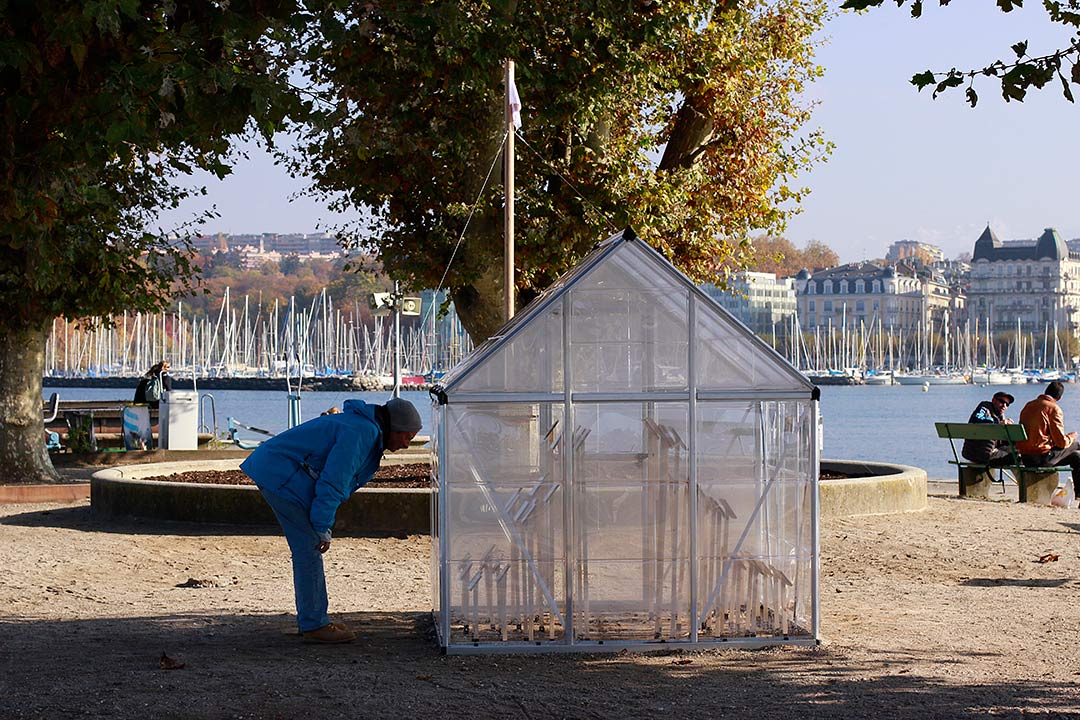 Ministère des Affaires de la Terre, Bains des Pâquis, Genève. Vue d'une personne penchée lisant les phrases dans la serre. Derrière, mat et pavillon sur esplanade d'herbe. Art participatif, Viviane Rabaud